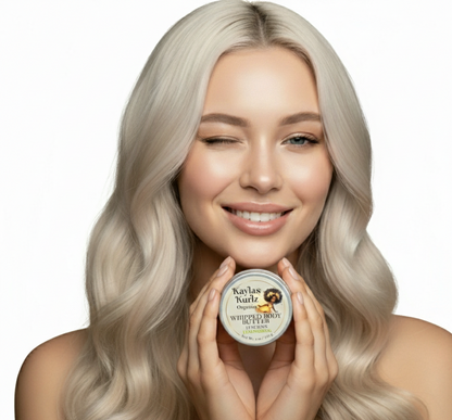 A beautiful woman with loose long curly hair winking her one eye  holding a  jar of Luscious Lemongrass Whipped Body Butter with a light, creamy texture, gently swirled on top. The packaging features a clean, natural design.